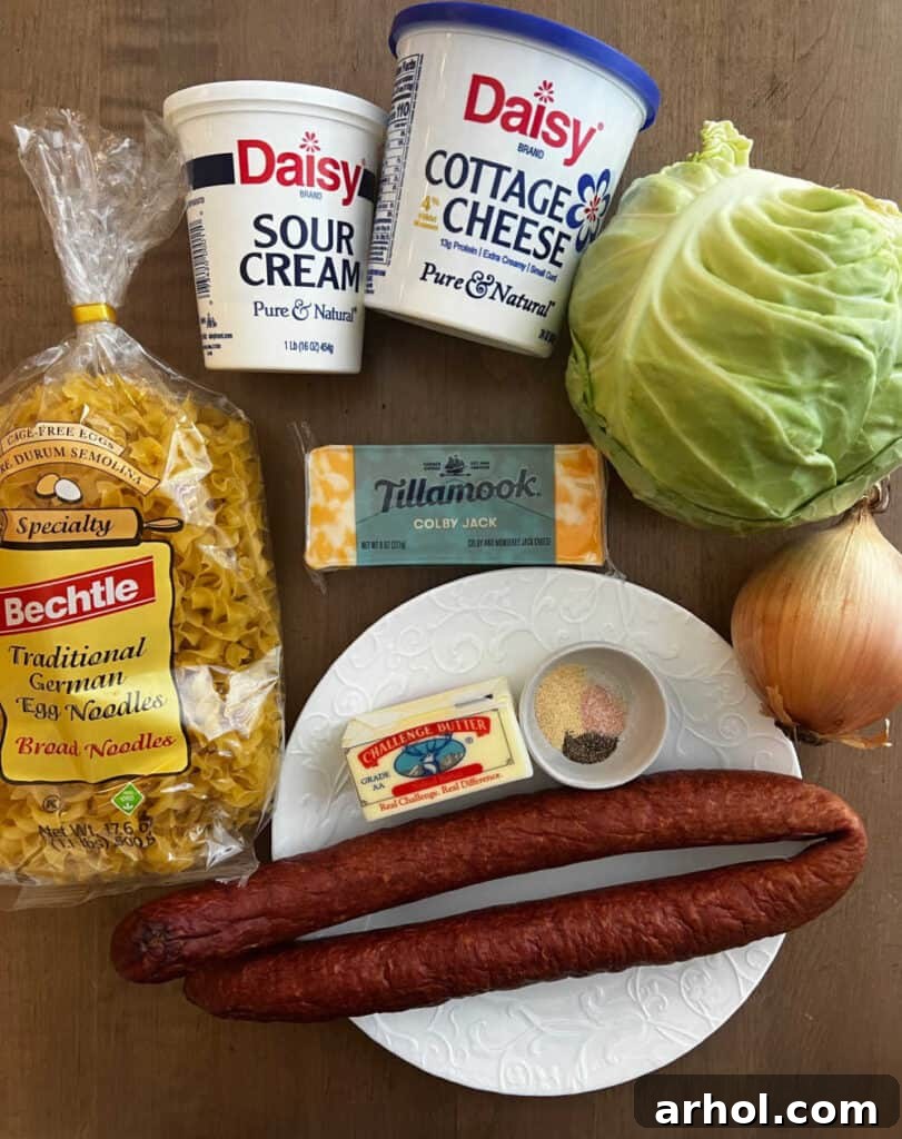 A flat lay photograph showcasing the main ingredients: smoked kielbasa, egg noodles, sour cream, cottage cheese, fresh cabbage, cheese, butter, onion, and various seasonings.
