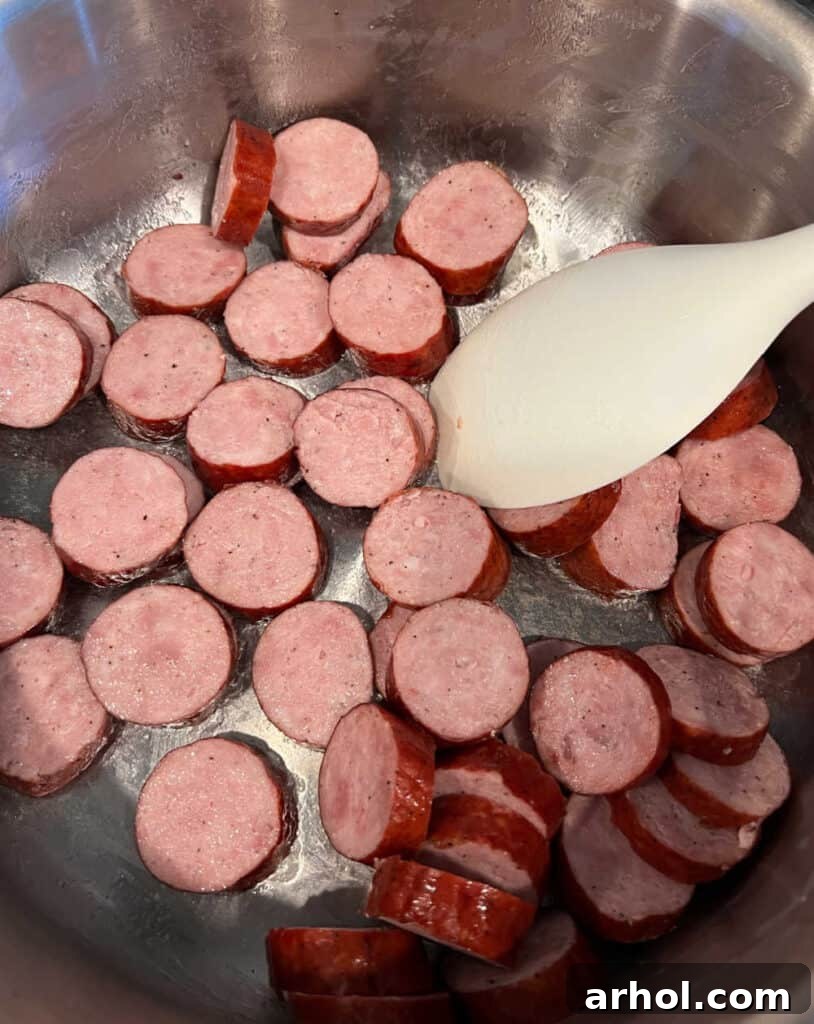 Sliced smoked sausage browning on the stovetop in a large pan.