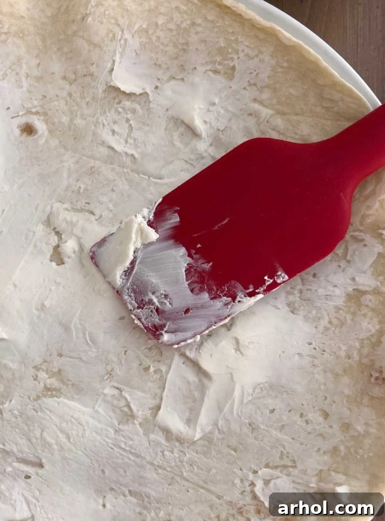 Festive Pinwheel Bites 4 spreading cream cheese smoothly onto a flour tortilla with a red spatula