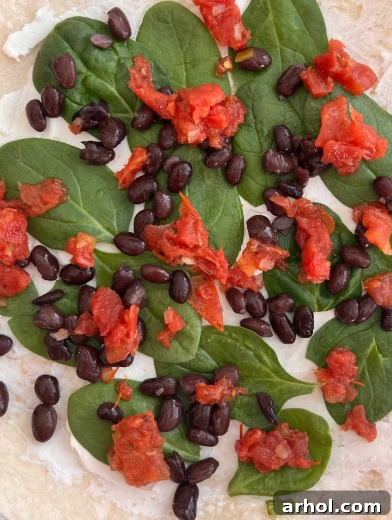 Festive Pinwheel Bites 5 layers of spinach leaves, black beans, and Rotel tomatoes spread over cream cheese on a tortilla