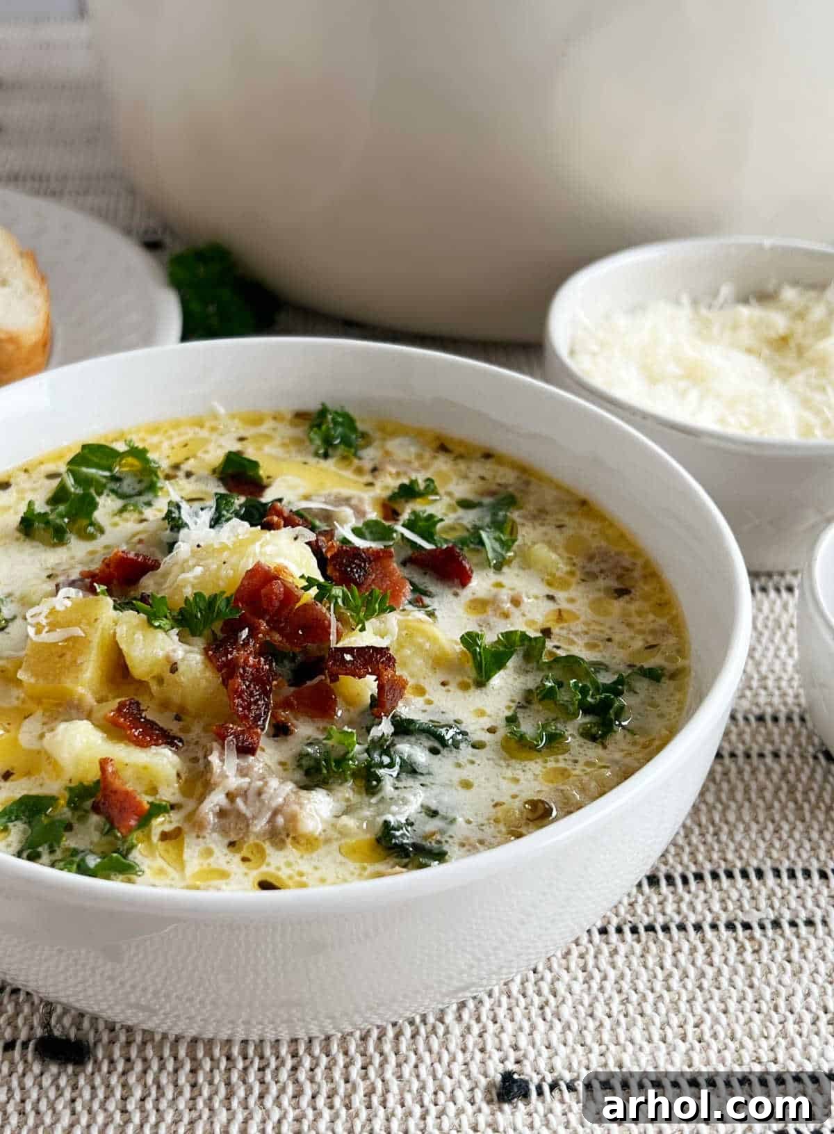 A steaming bowl of homemade Zuppa Toscana soup, brimming with potatoes, sausage, bacon, and kale, garnished with fresh parsley.