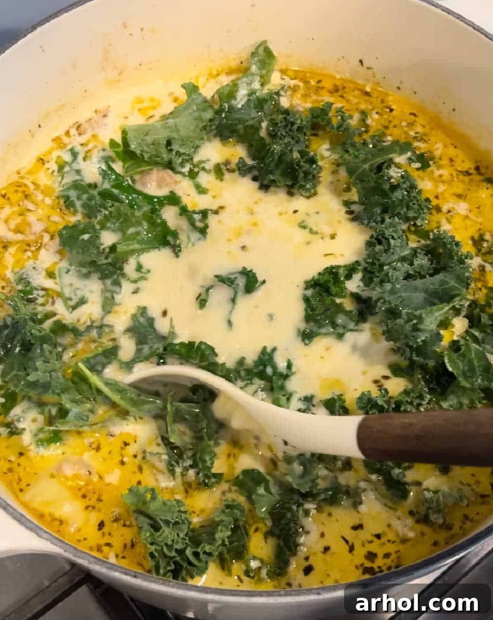 Stirring heavy cream and fresh chopped kale into the simmering Zuppa Toscana soup.