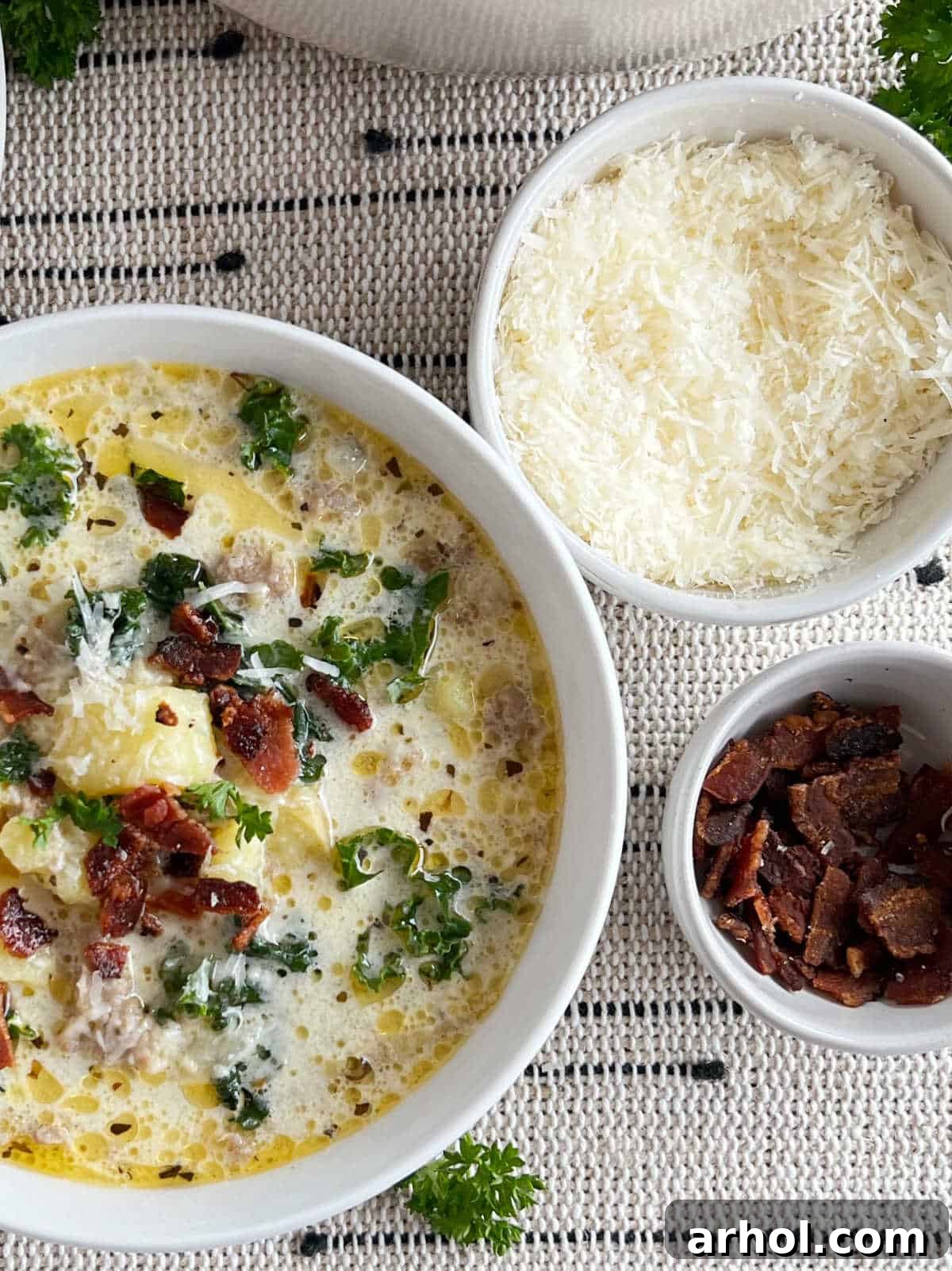 A beautifully presented bowl of Zuppa Toscana soup, garnished with grated Parmesan cheese and crispy bacon bits, ready to eat.