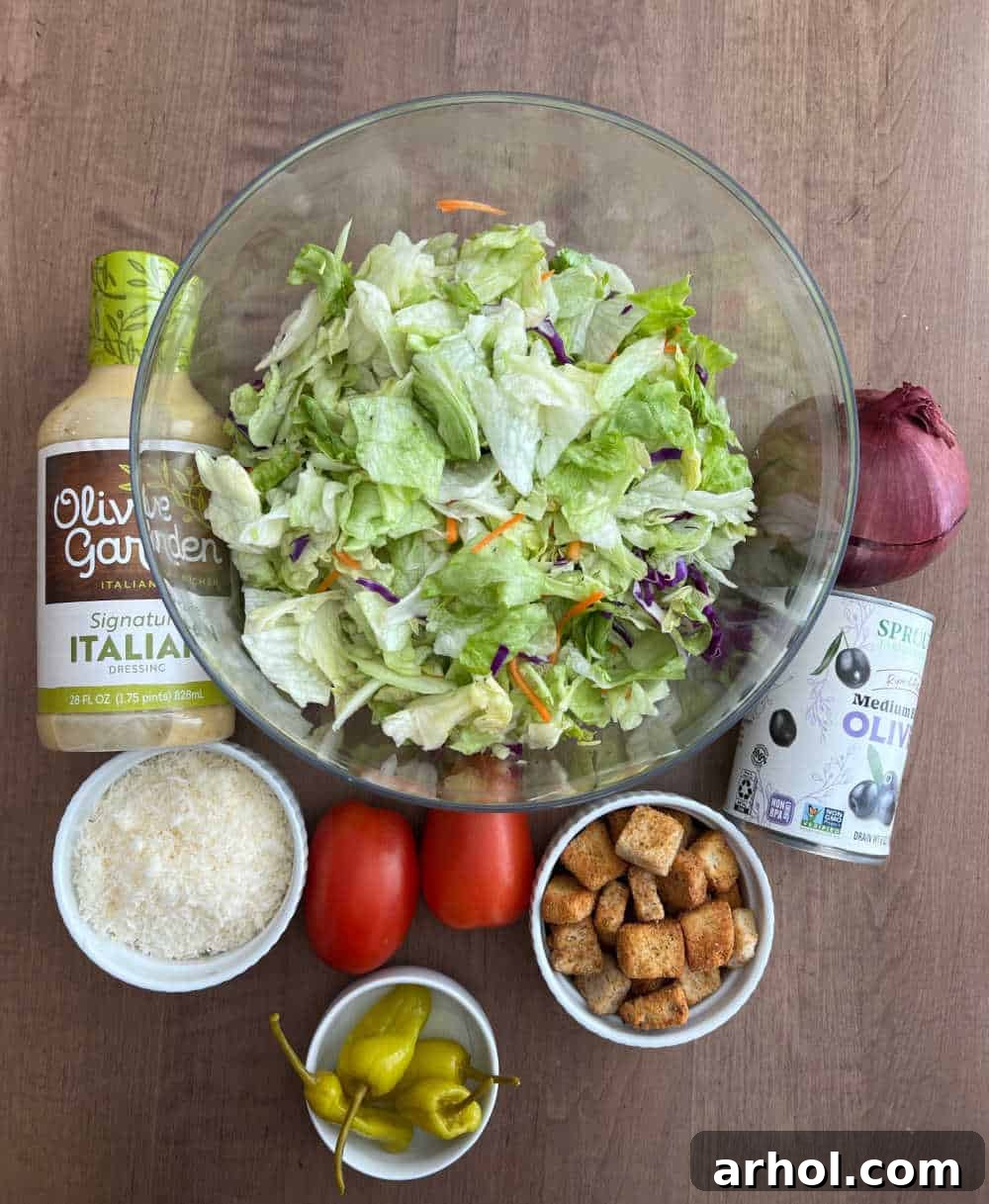 A vibrant flat lay shot displaying all the fresh ingredients for a copycat Olive Garden salad: crisp iceberg lettuce, a bottle of creamy Italian dressing, grated Parmesan cheese, bright red Roma tomatoes, briny black olives, thinly sliced red onion, and tangy pepperoncini peppers, all neatly arranged.
