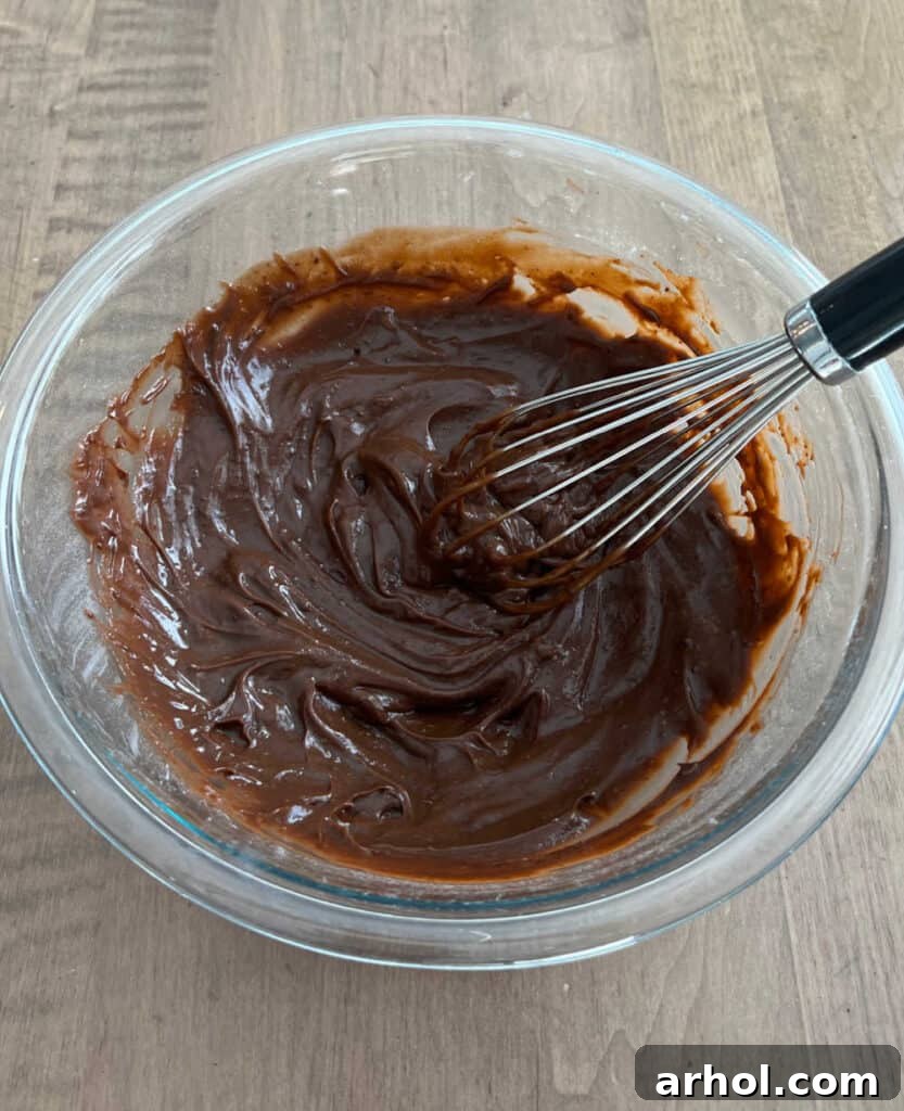 A person whisking instant chocolate pudding mix and cold milk in a large mixing bowl until thick and smooth.