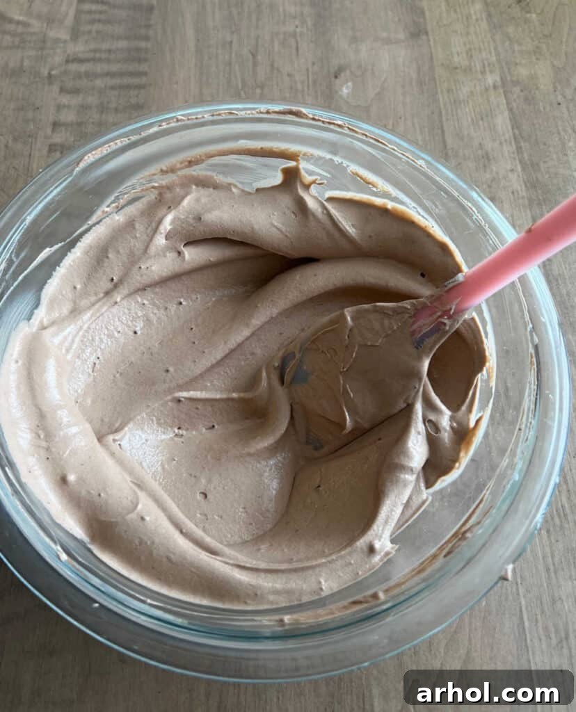 A rubber spatula gently folding thawed Cool Whip into the chocolate pudding mixture in a mixing bowl.