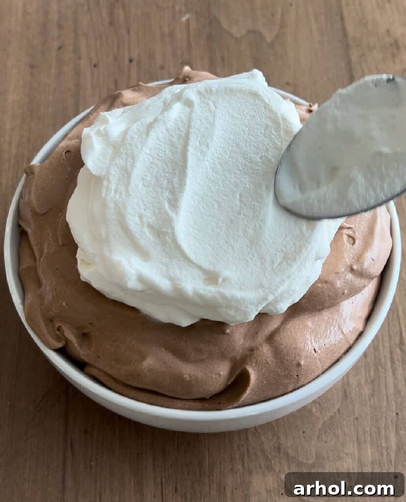 Whipped topping being spread over the chocolate pie dip in a bowl, before the final chocolate chip garnish.
