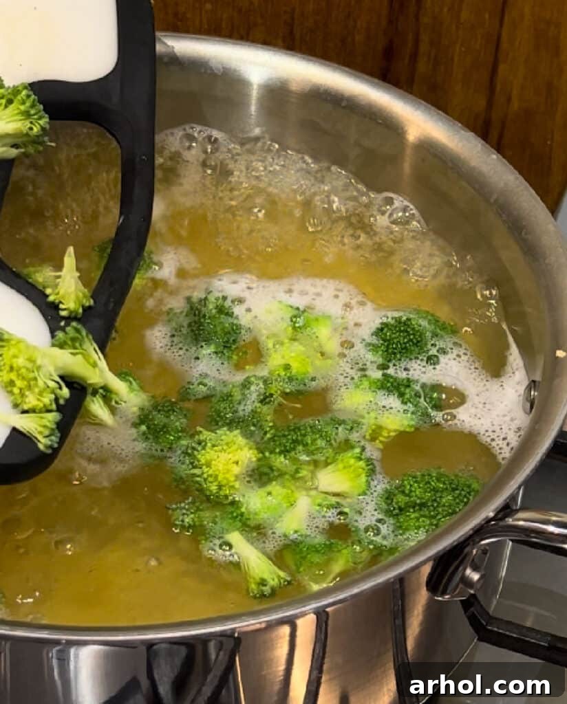 Penne pasta and fresh broccoli florets cooking together in a pot of boiling, salted water, preparing for the casserole.
