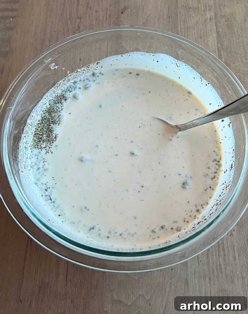 A mixing bowl with creamy Alfredo sauce, half and half, and seasonings being stirred with a whisk, creating a smooth, flavorful base for the casserole.