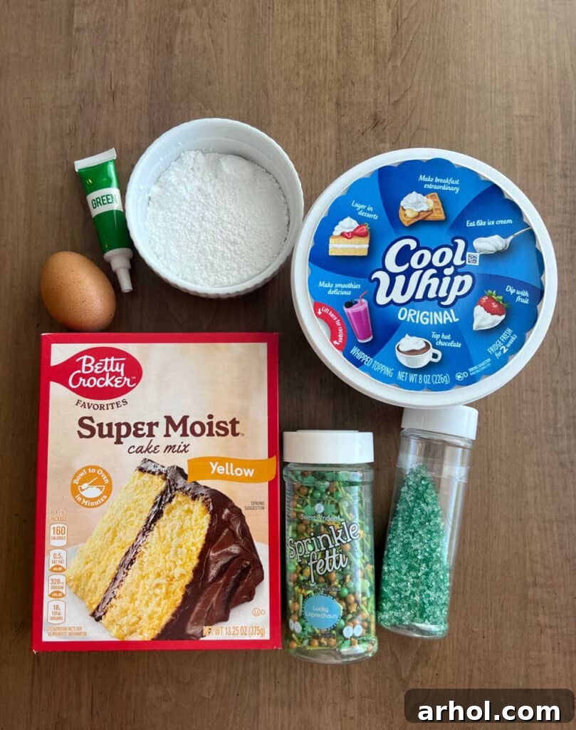 A flat lay showcasing all the simple ingredients required for St. Patrick's Day cookies: yellow cake mix, a tub of Cool Whip, an egg, green food coloring, and a bowl of powdered sugar.