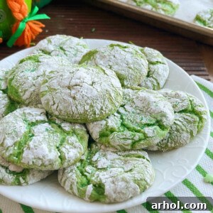 A close-up of festive St. Patrick's Day green crinkle cookies on a white plate, showcasing their perfect texture and powdered sugar coating.