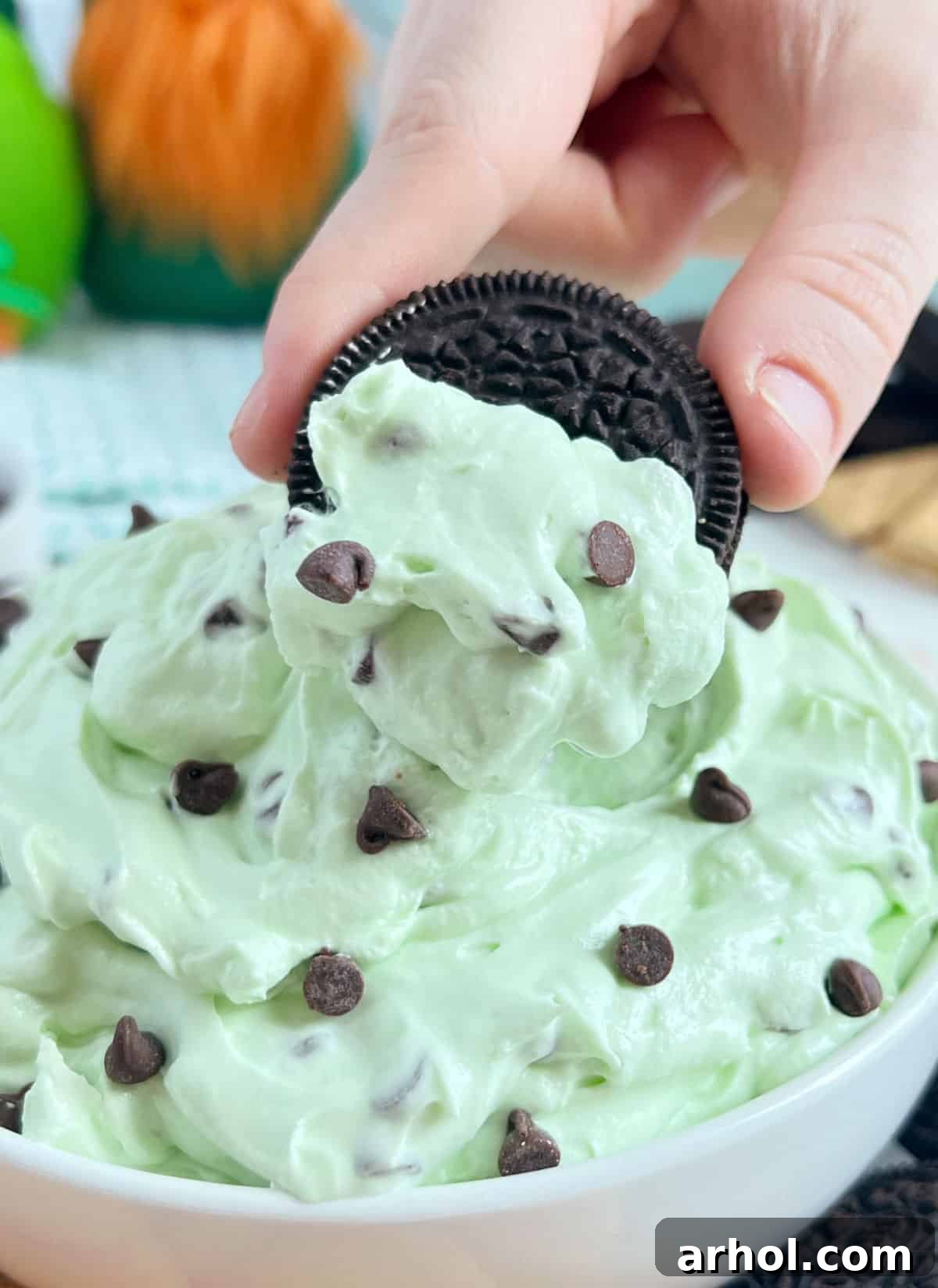 A close-up of a mint Oreo cookie being dipped into the vibrant green mint chocolate chip cheesecake dip, highlighting its creamy texture.
