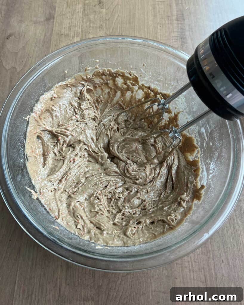 A close-up shot of cookie dough being mixed in a bowl with an electric mixer, showing its smooth, combined texture.