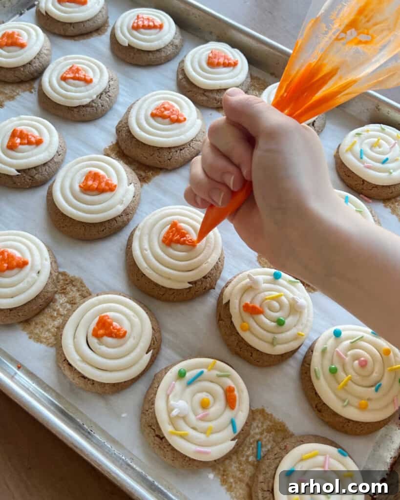 Detailed shot of hands piping delicate orange carrots with green tops onto freshly frosted carrot cake cookies, showcasing artistic decoration.
