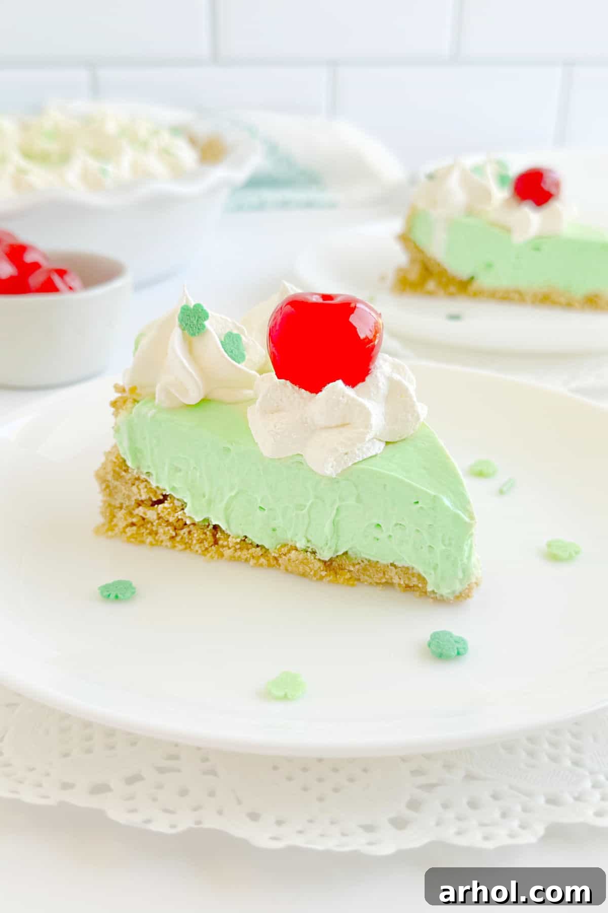 A vibrant green slice of no-bake shamrock shake pie, generously topped with fluffy whipped cream and a bright red maraschino cherry, ready to be enjoyed on St. Patrick's Day.