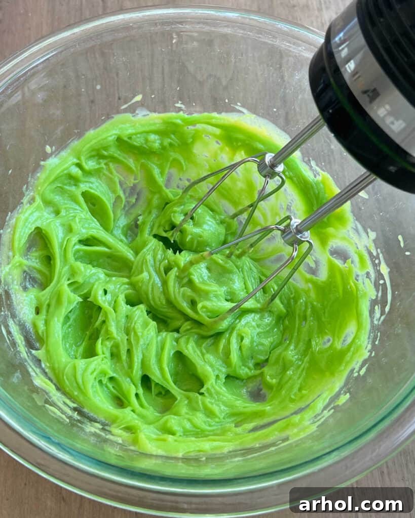 A vibrant green pie filling being mixed in a bowl with an electric mixer, ensuring the color and flavor are perfectly incorporated.