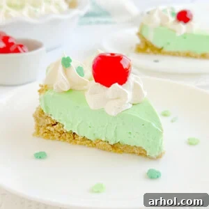 A beautiful slice of no-bake shamrock pie, featuring its creamy mint filling and graham cracker crust, topped with a dollop of whipped cream and a maraschino cherry.