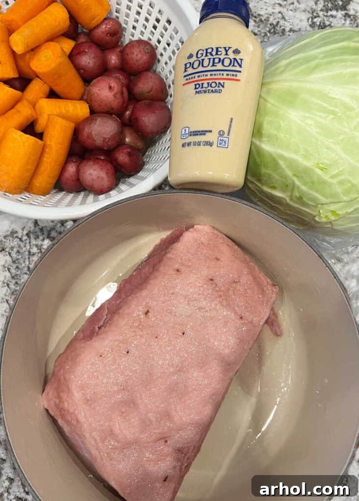 Flat cut corned beef, fresh carrots, small red potatoes, Dijon mustard, and a head of green cabbage laid out as ingredients.