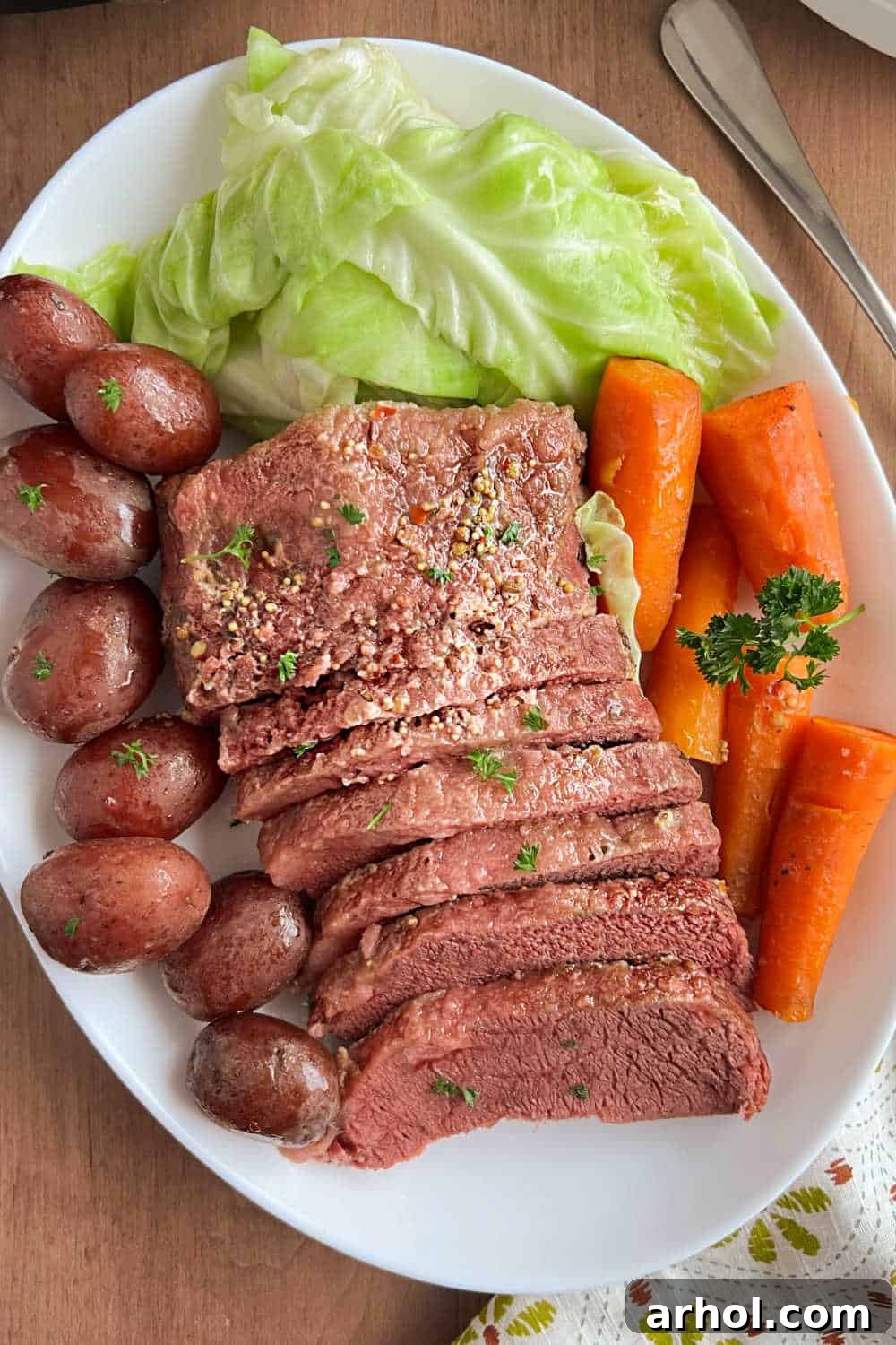 Sliced corned beef brisket with baby red potatoes, green cabbage, and carrots beautifully arranged on a platter for serving.
