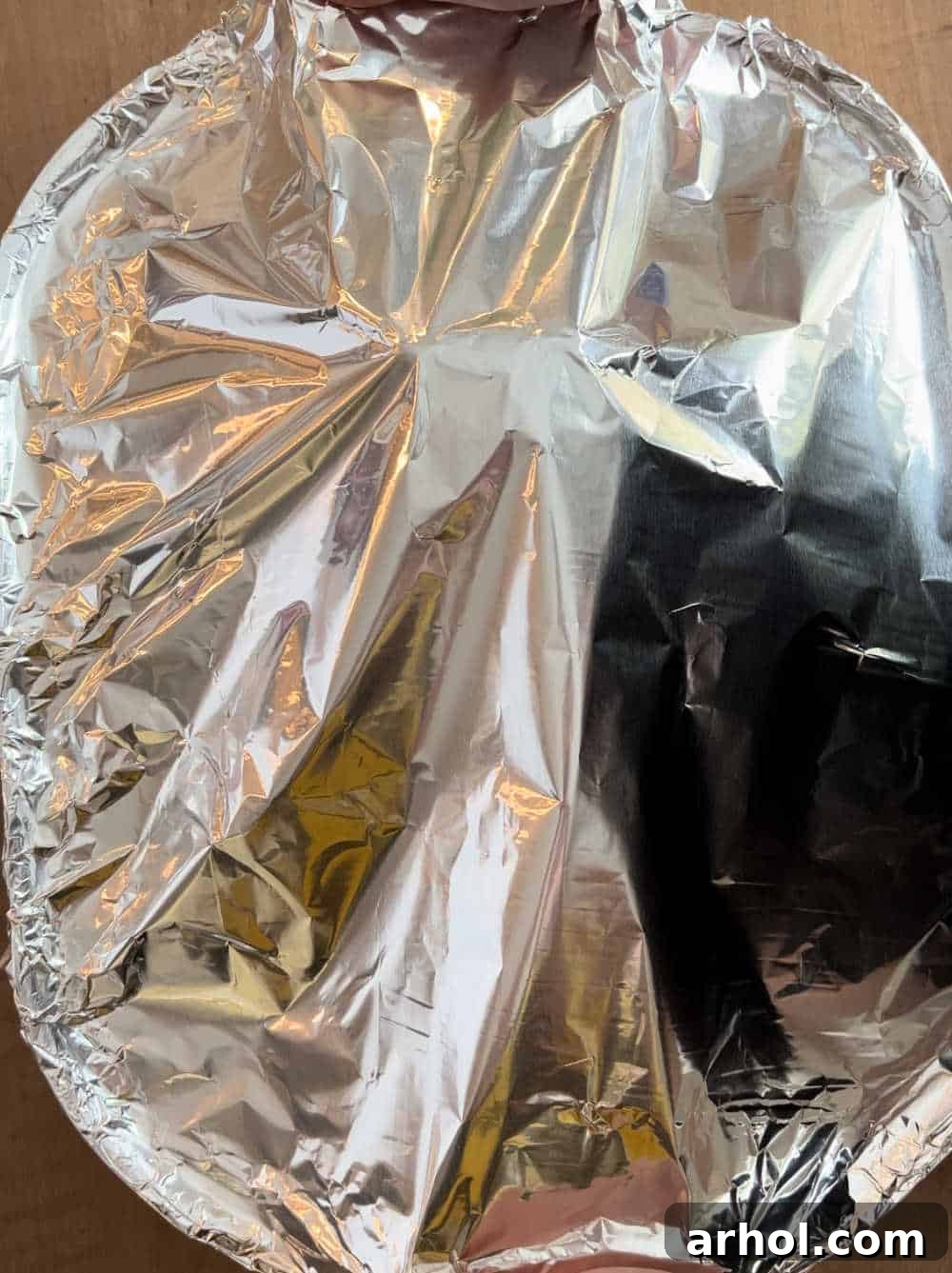A spiral-cut ham tightly covered with aluminum foil in a roasting pan, inside the oven.