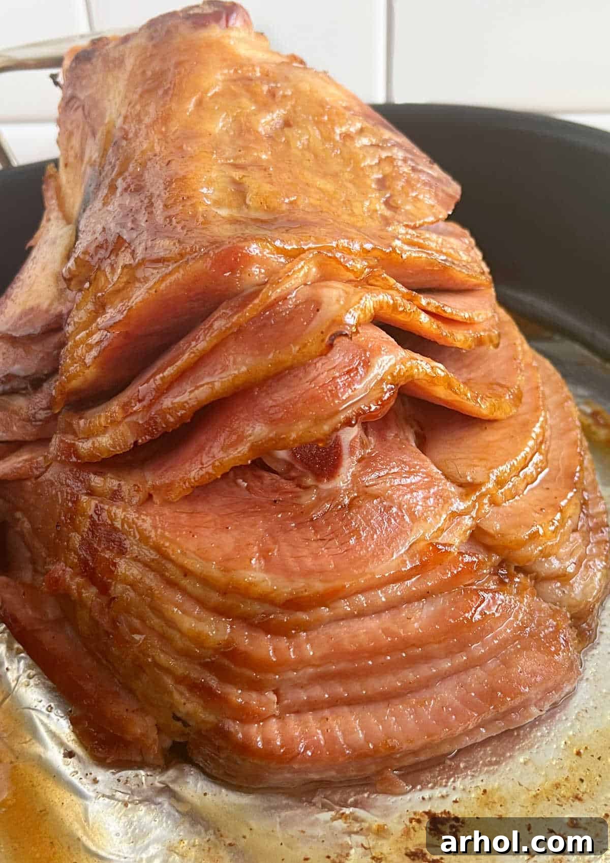 A baked spiral-cut ham with Dr. Pepper glaze, resting in a roasting pan before serving.