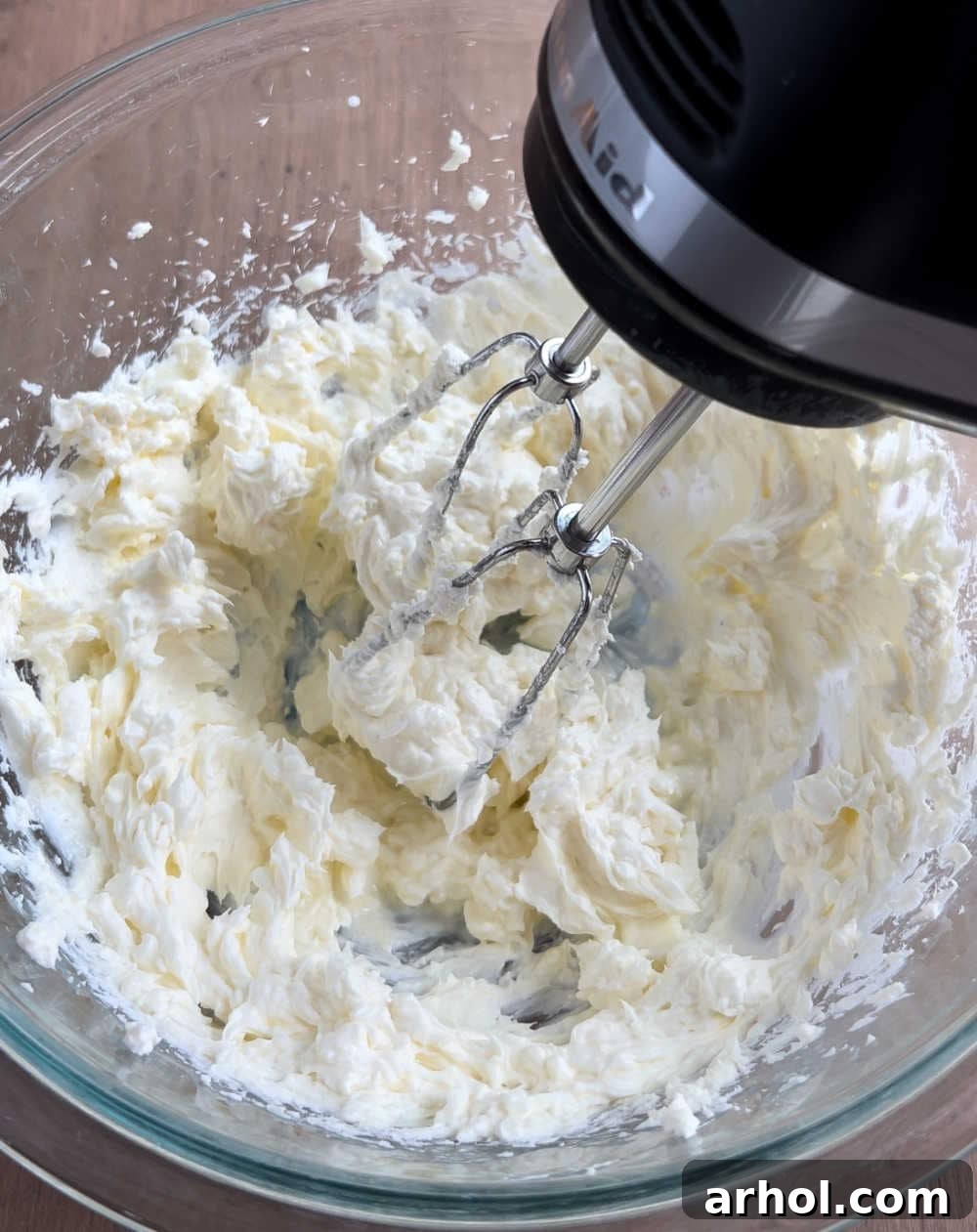 Mixing softened cream cheese in a large bowl with an electric mixer until smooth and creamy, preparing the base for the cheesecake dip.