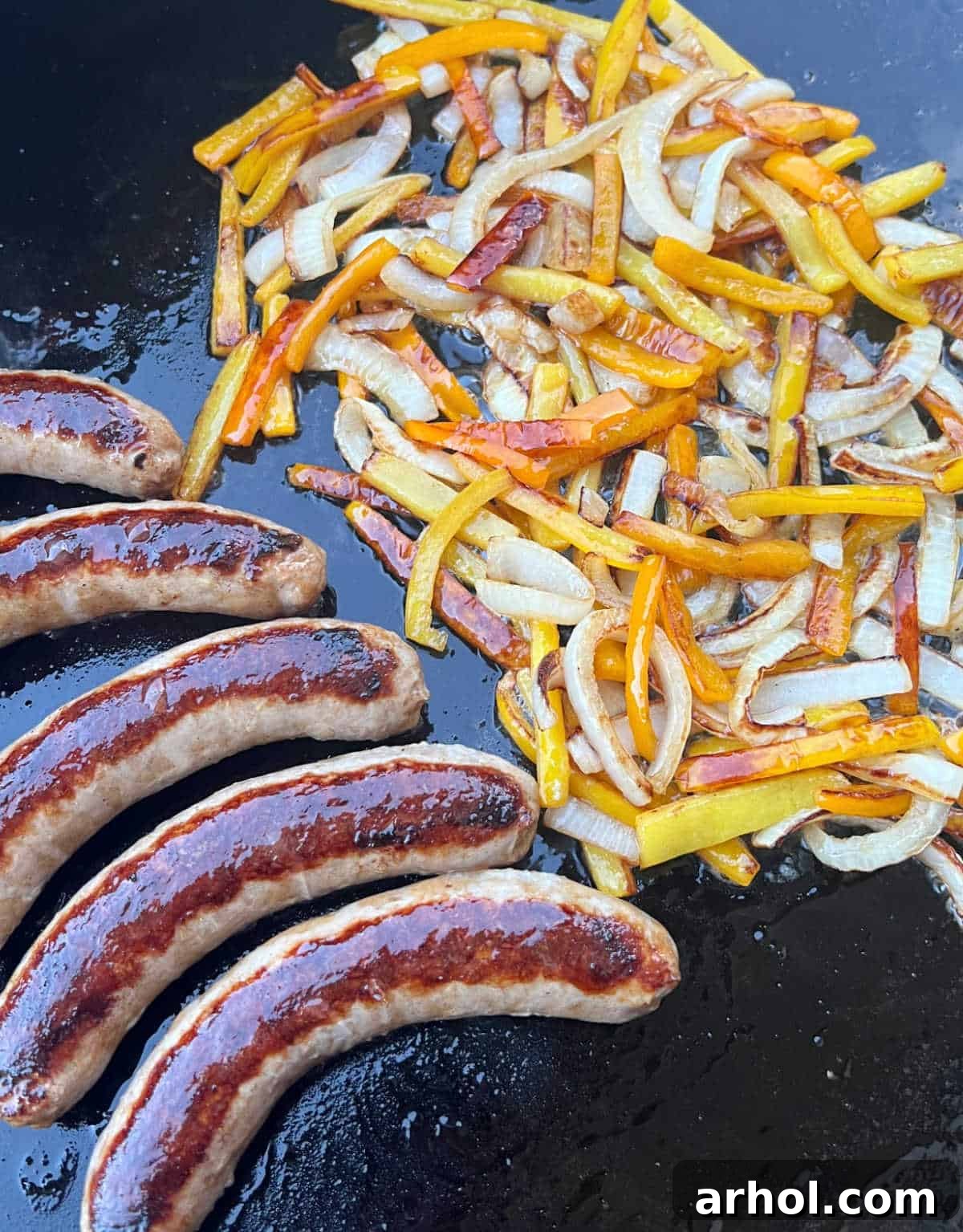Sizzling Italian sausages and colorful bell peppers with onions on a Blackstone Griddle, ready to be served as a delicious meal.