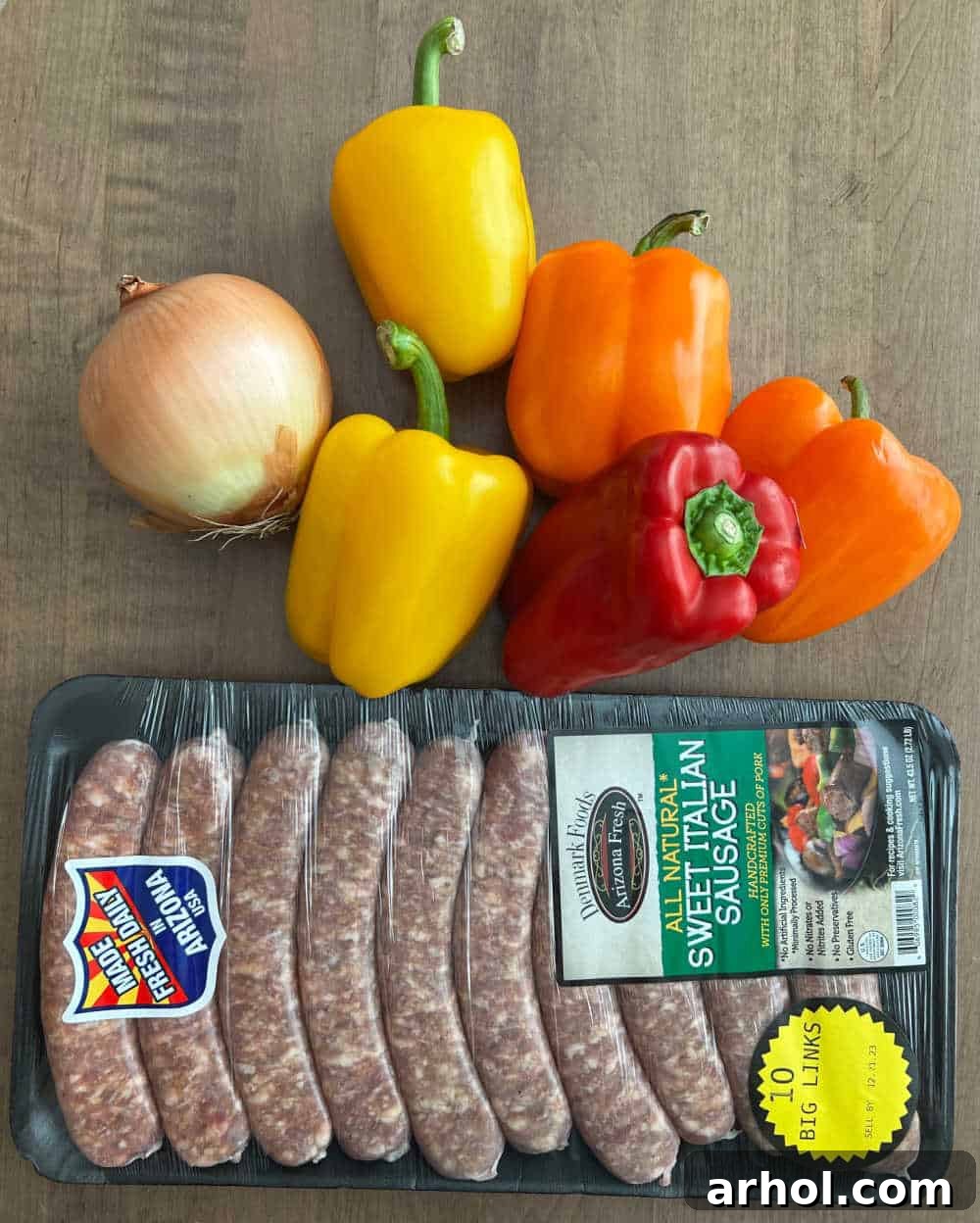 Fresh Italian sausage links, vibrant bell peppers in red, yellow, and orange, and a neatly sliced white onion, all prepped for cooking on the griddle.