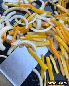 Bell peppers and onions caramelizing on the griddle next to sausages.