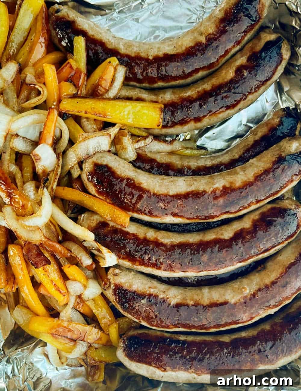 Cooked Italian sausages, vibrant peppers, and tender onions held warm in a foil pan, ready for serving.