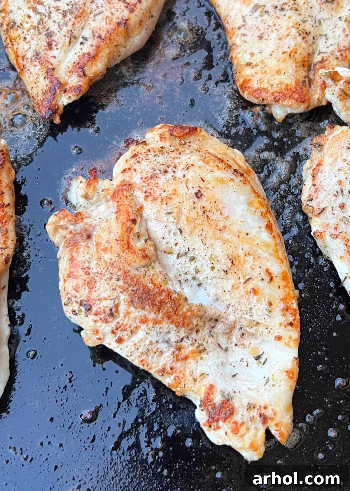 Perfectly seared chicken breasts cooking on a hot Blackstone griddle with visible golden-brown crust and steam rising.