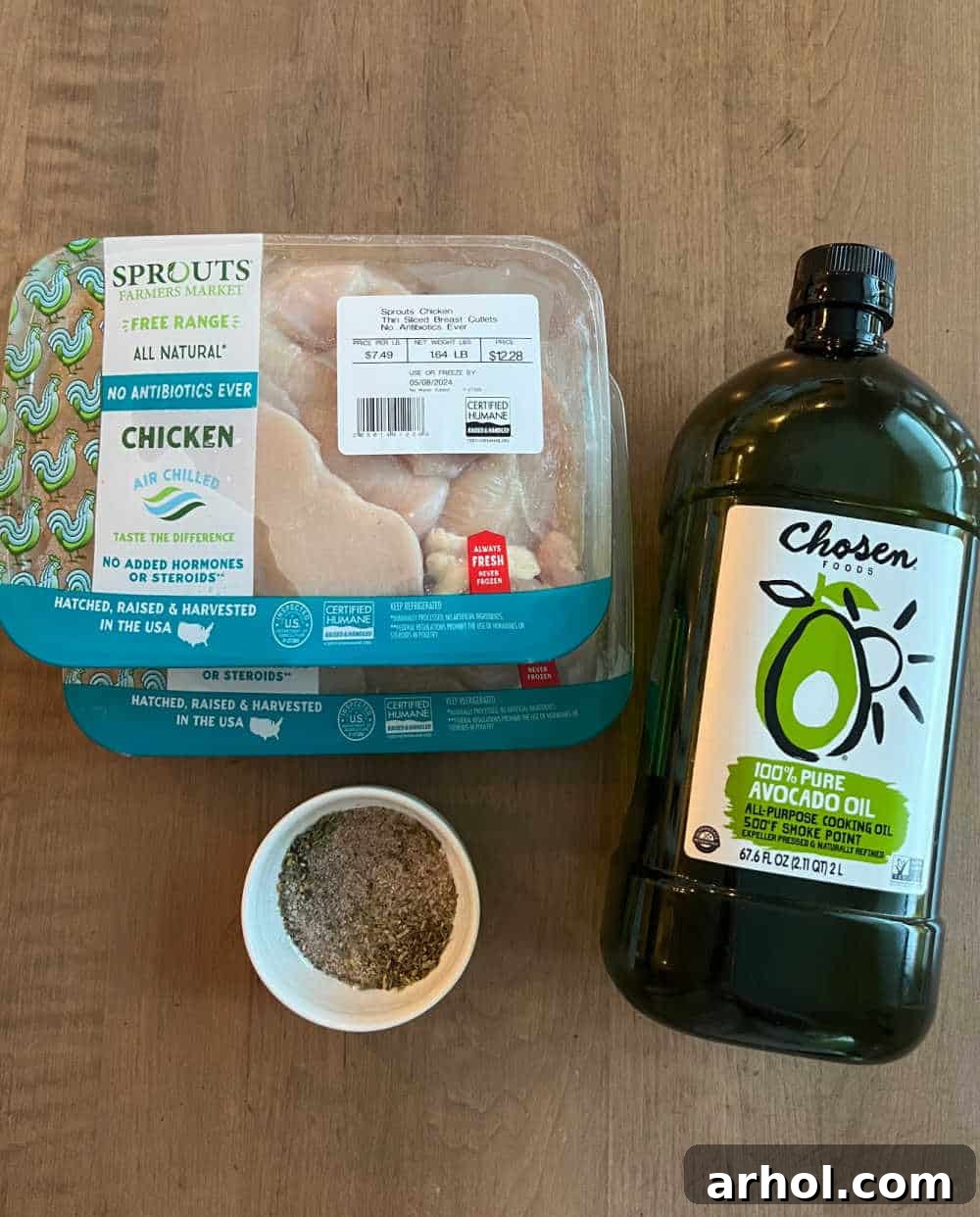 Fresh chicken breast cutlets, a bottle of avocado oil, and bowls of sea salt, black pepper, and Italian seasoning laid out on a wooden cutting board.