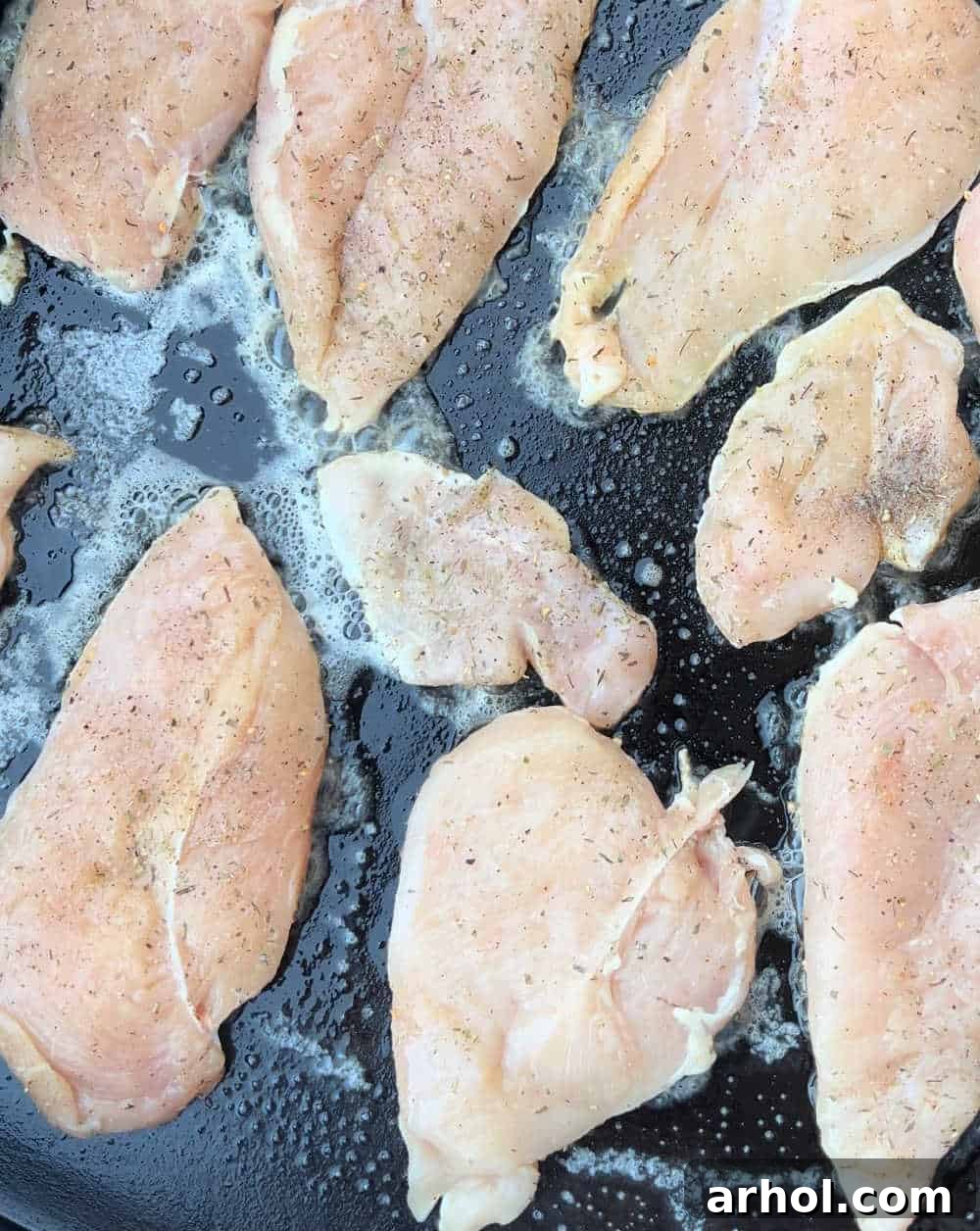 Seasoned chicken breast cutlets cooking on a hot flat top grill, showing early searing and browning.