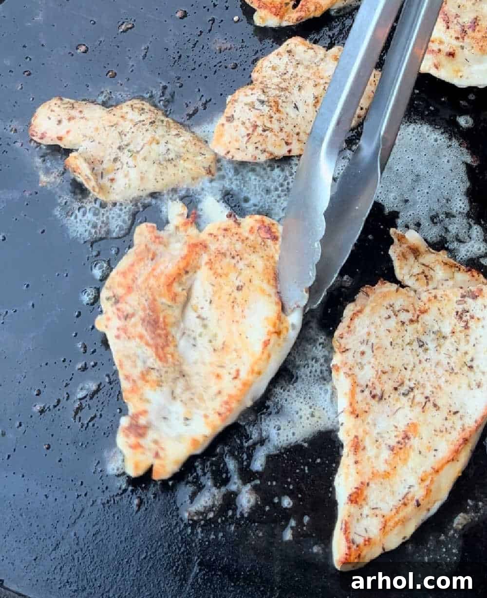 Using tongs to expertly flip a perfectly seared chicken breast cutlet on the Blackstone griddle, revealing a golden crust.