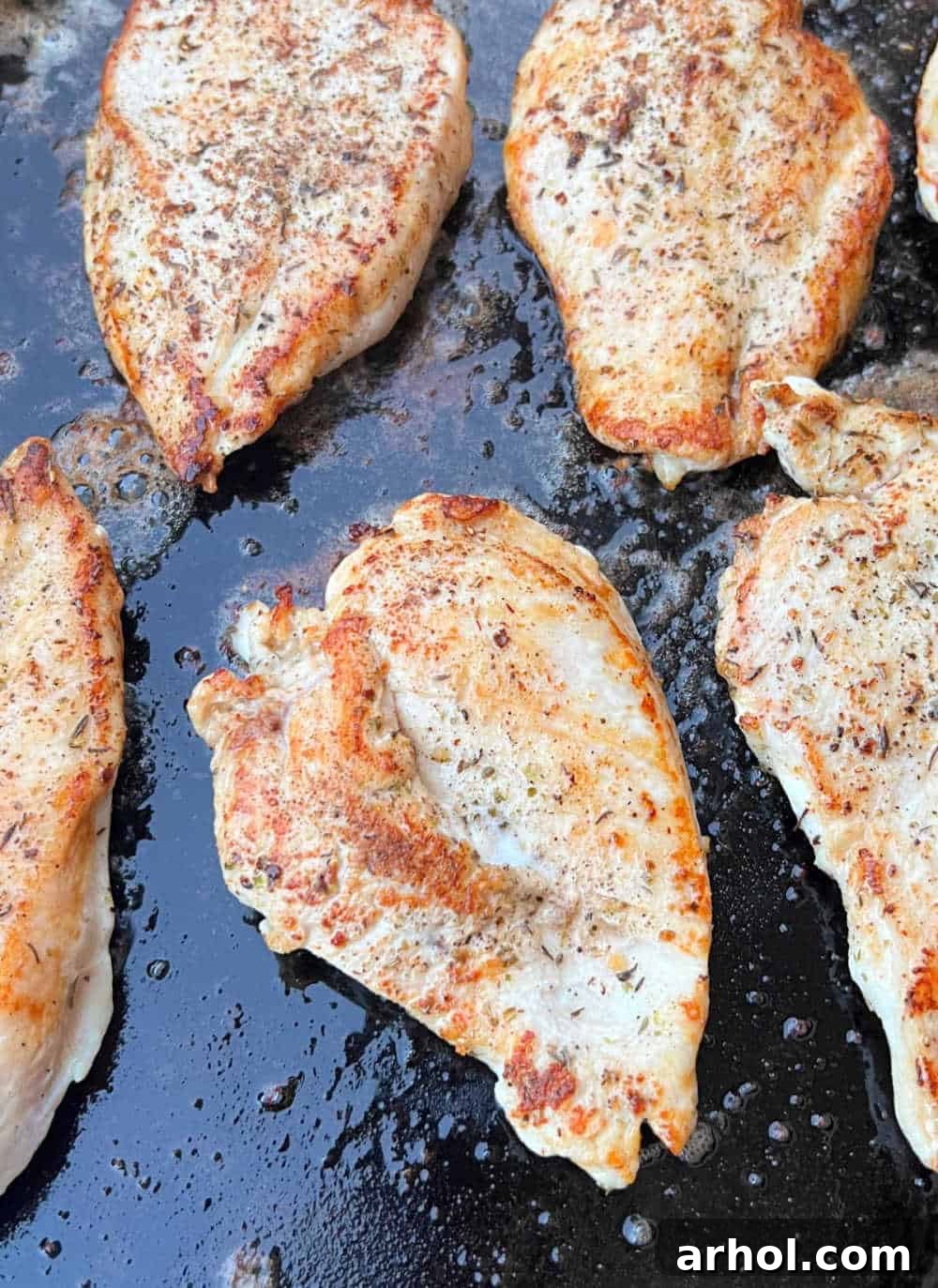 Close-up of golden brown seared chicken breasts with perfect grill marks resting on a Blackstone griddle, ready to be served.