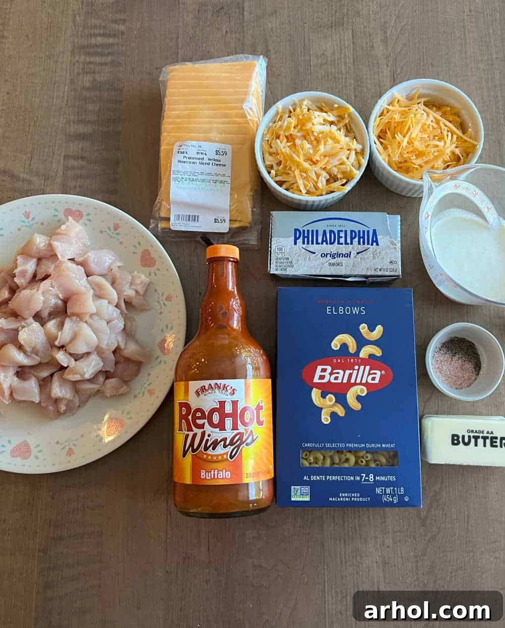 Arrangement of main ingredients for Buffalo Chicken Mac and Cheese: cubed chicken, Buffalo wing sauce, elbow macaroni, a variety of cheeses, cream cheese, heavy cream, butter, and spices.