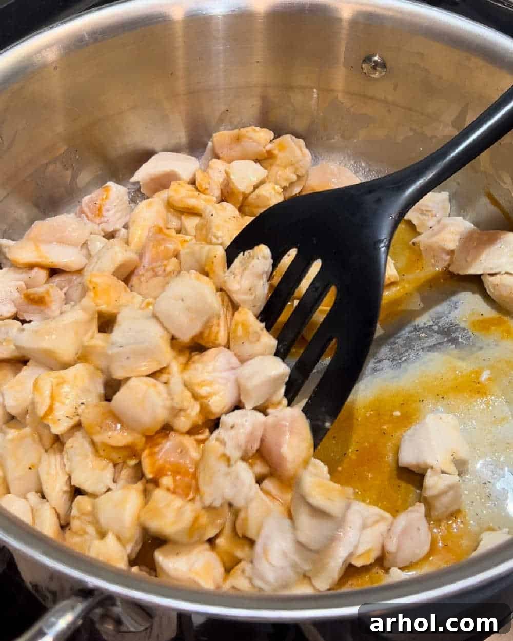 Close-up shot of bite-sized chicken pieces cooking in a pot with butter and Buffalo sauce.