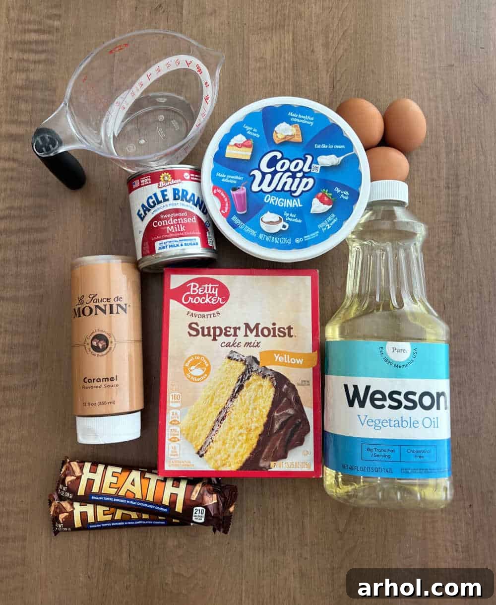 Various ingredients for Heath bar cake including cake mix, Heath bars, eggs, oil, water, condensed milk, Cool Whip, and caramel sauce, neatly arranged.