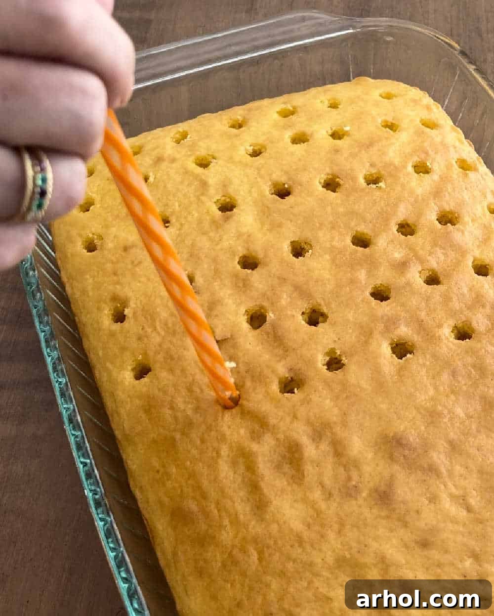 Using a large drinking straw to poke holes evenly into the warm baked cake.