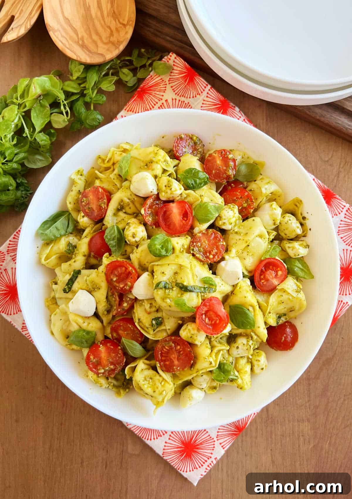 A vibrant bowl of tortellini pasta salad with fresh pesto, halved cherry tomatoes, and mozzarella pearls, garnished with fresh basil leaves, ready to be served.