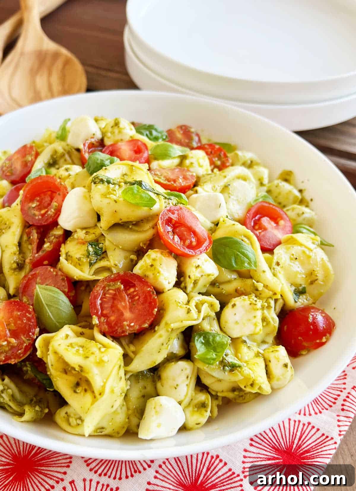 A beautiful tortellini pesto pasta salad served in an elegant white bowl on a rustic wooden table, garnished with fresh basil, ready for a summer meal.
