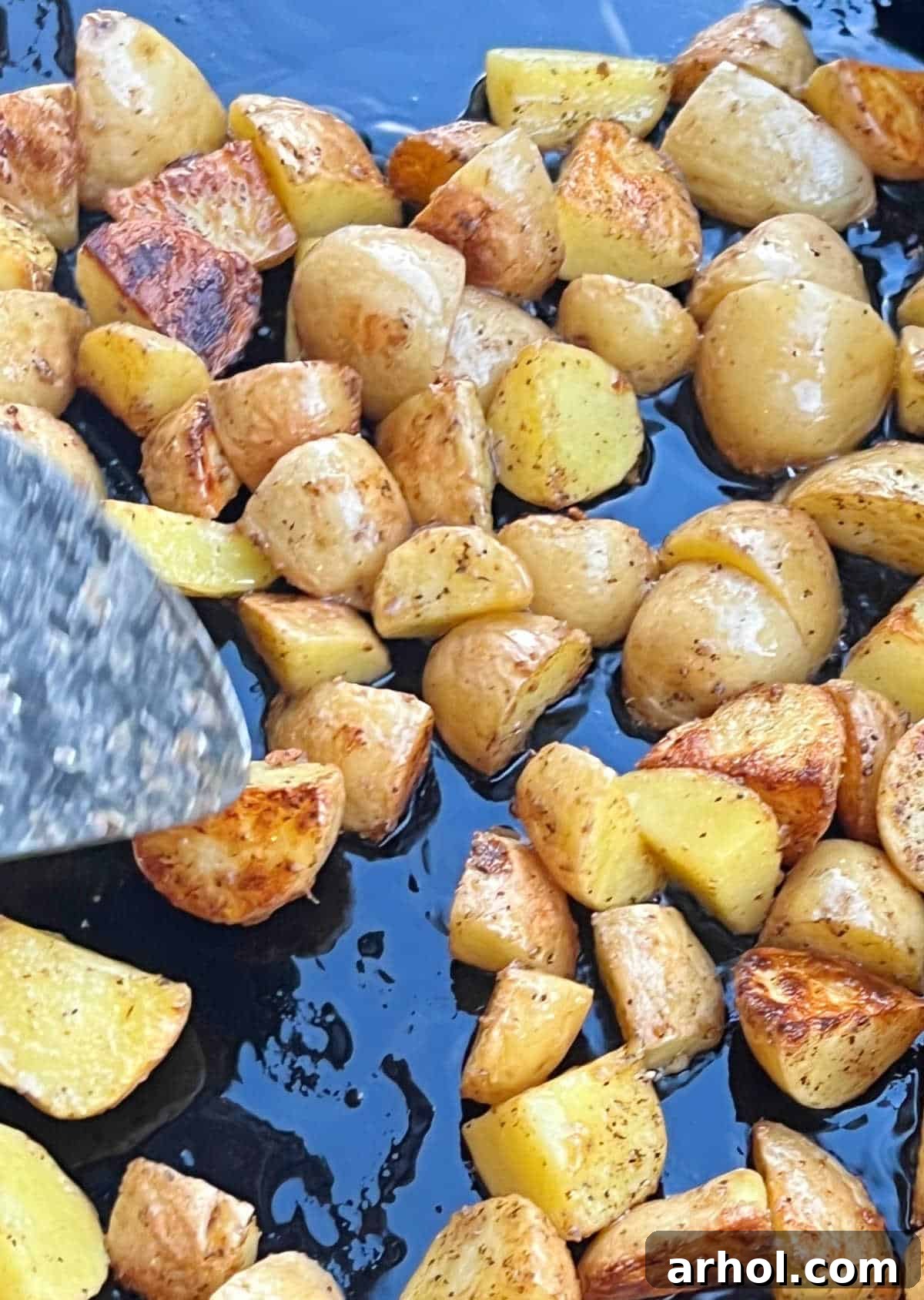 Sizzling Spuds The Blackstone Way 5 A chef using a grilling spatula to toss and turn golden-brown fried potatoes on a Blackstone griddle.