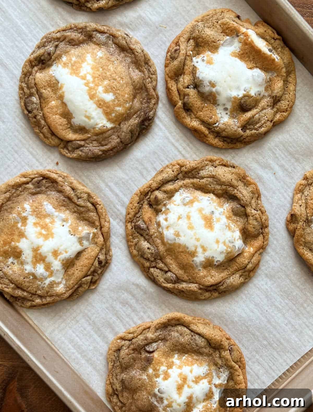 Freshly baked S'mores cookies with melted marshmallow centers cooling on a baking sheet, ready to be devoured.
