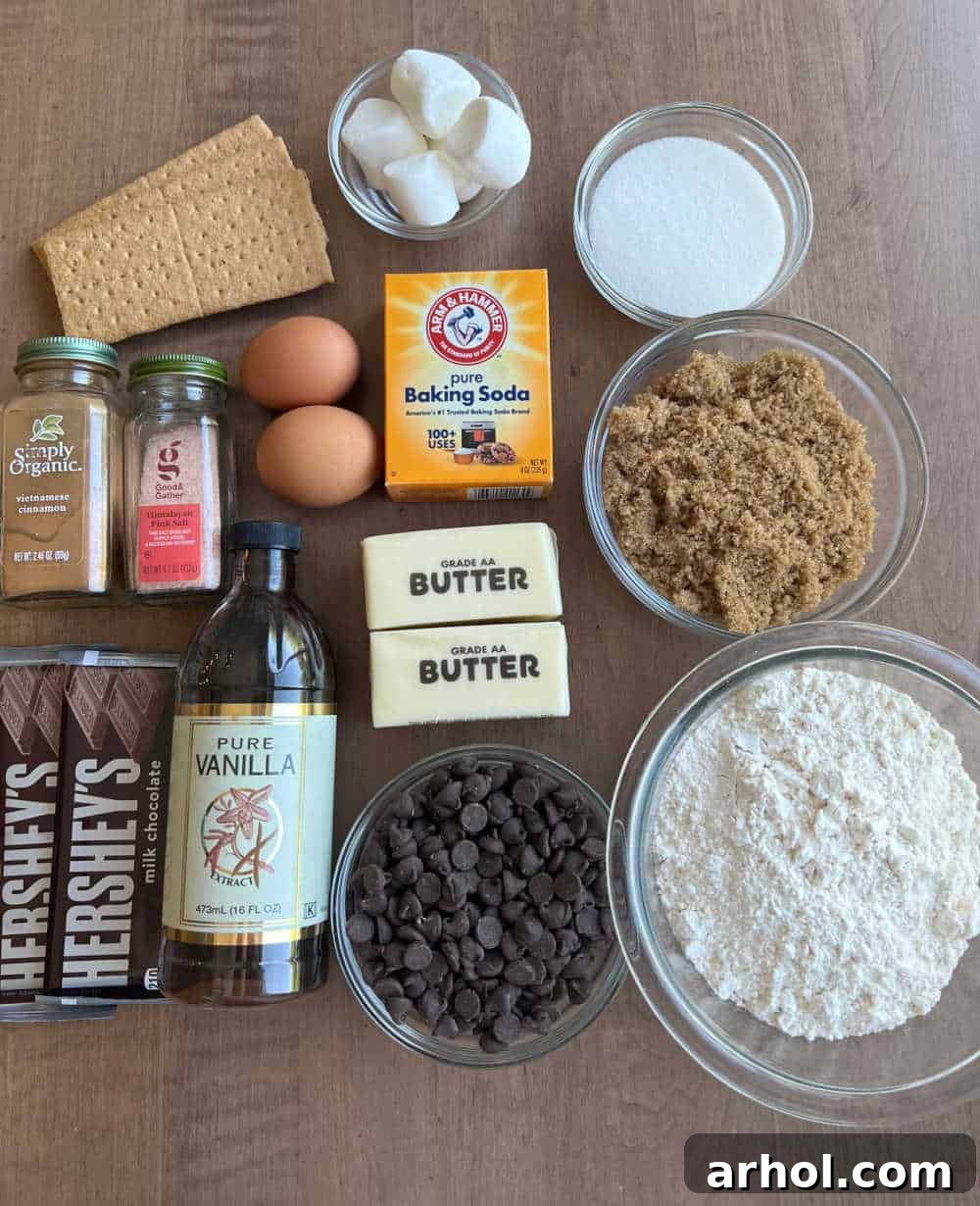 A flat lay photograph showcasing all the delicious S'mores cookie ingredients: chocolate chip cookie dough, graham crackers, Hershey's chocolate bars, and fluffy marshmallows.
