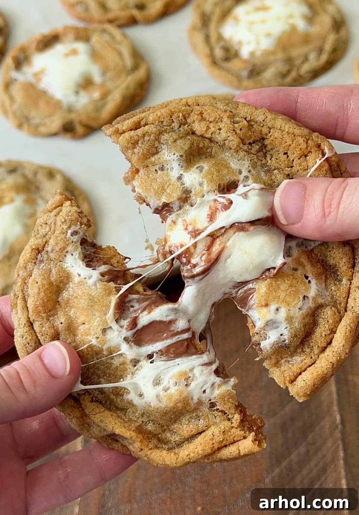 A baked S'mores cookie being gently pulled apart, revealing its irresistible gooey center with melted marshmallow and chocolate, still warm from the oven.