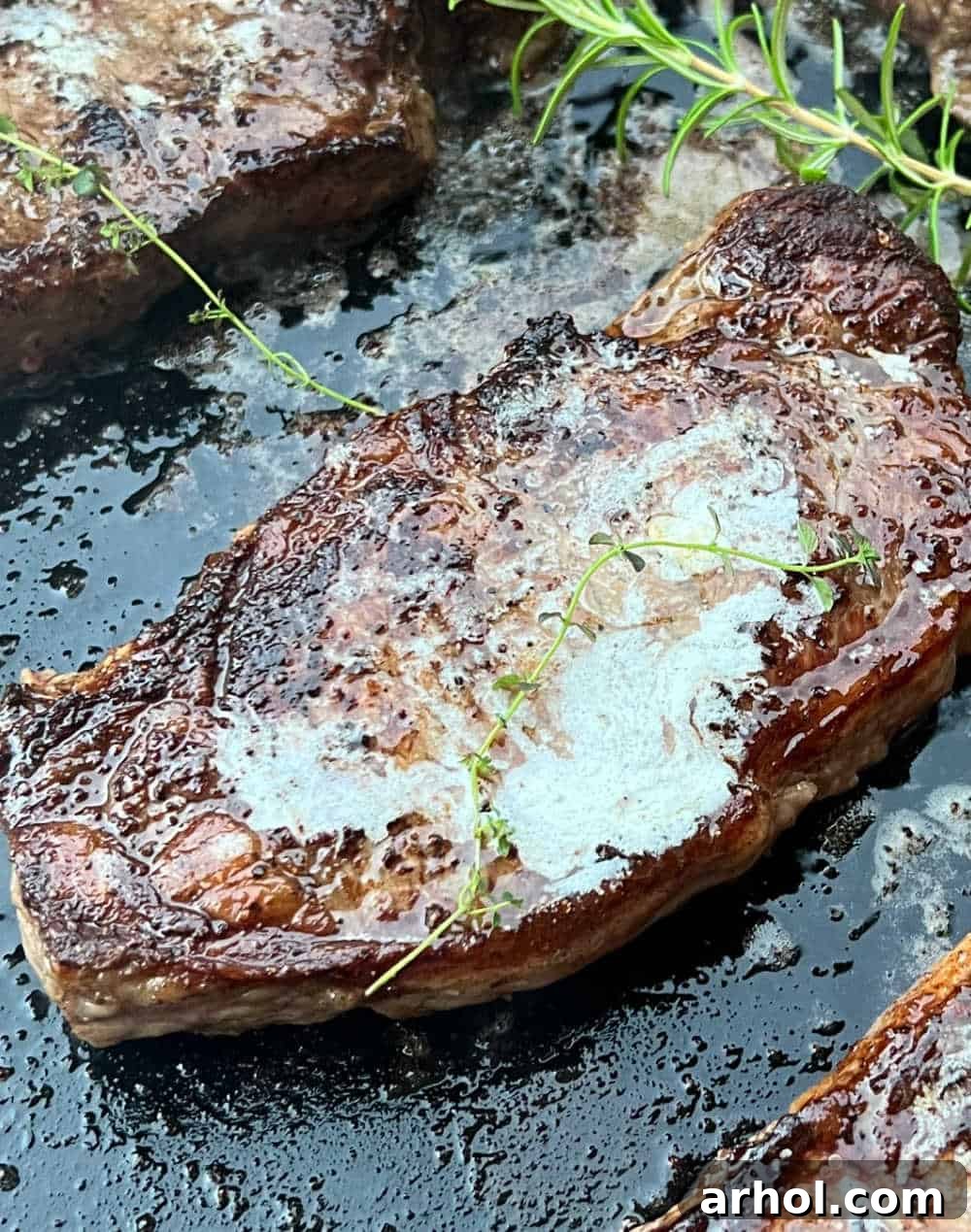 A New York strip steak, expertly seared on a Blackstone griddle, garnished with fresh sprigs of rosemary and thyme.
