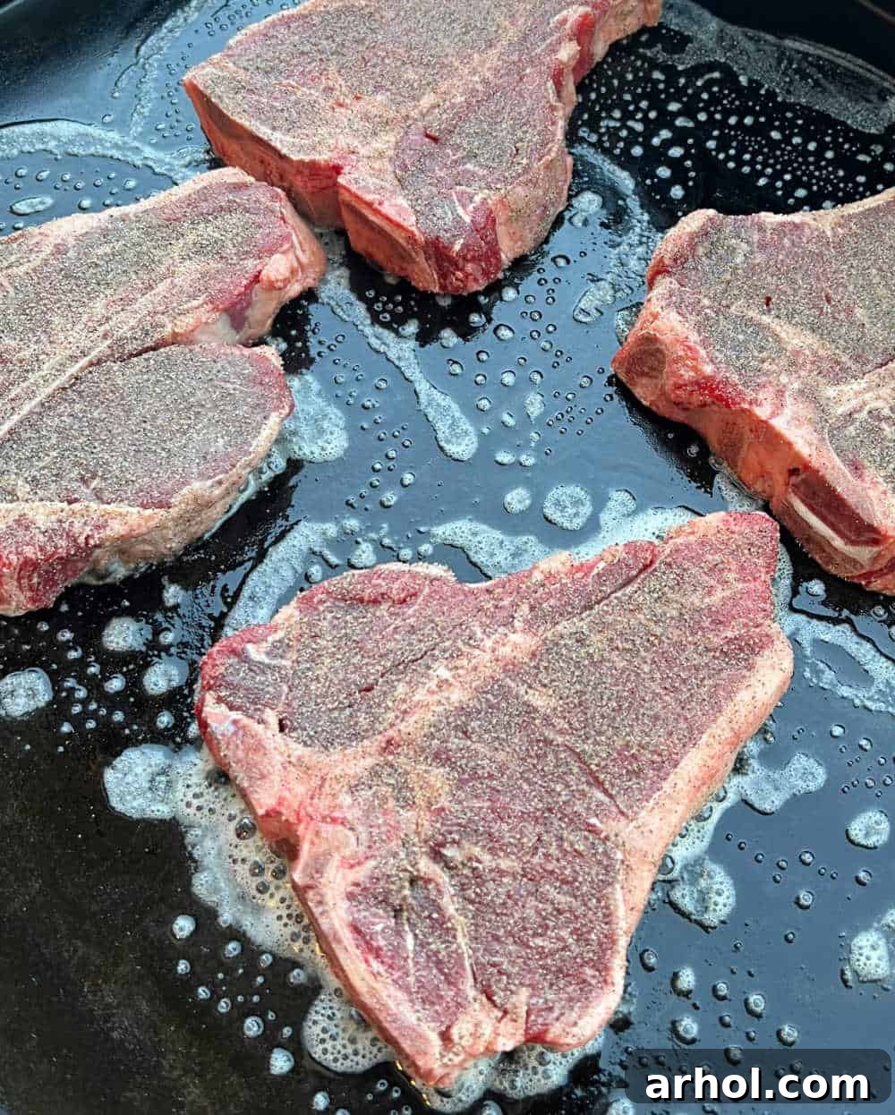 Four seasoned porterhouse steaks sizzling and developing a rich, dark crust on a hot Blackstone griddle.