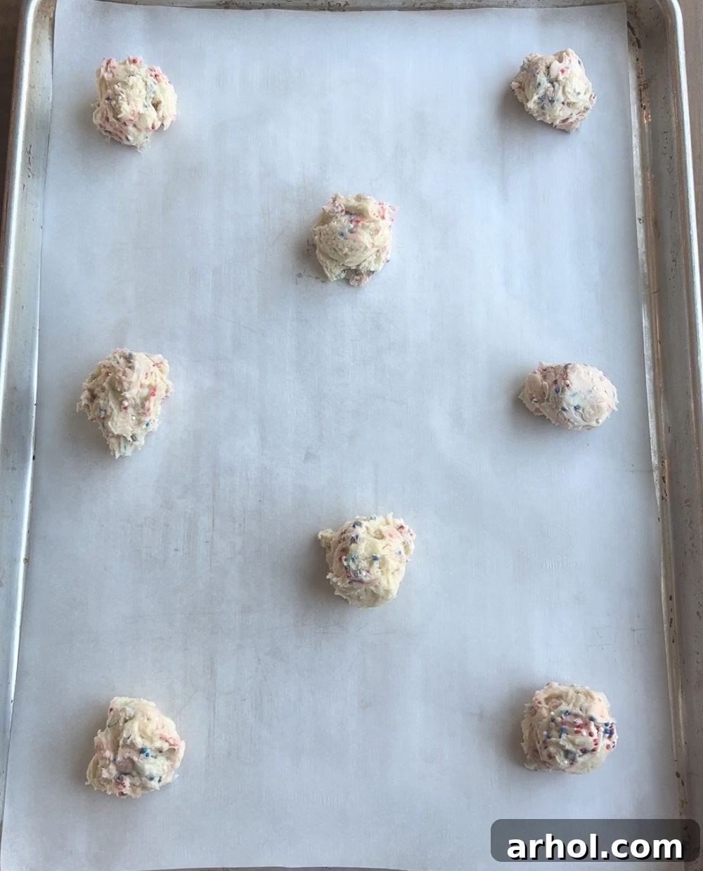 Scooped portions of patriotic cookie dough, perfectly spaced on a parchment-lined baking sheet, ready for baking.