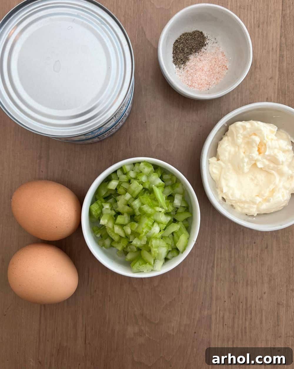 Essential ingredients for classic tuna salad: canned tuna, hard-boiled eggs, chopped celery, creamy mayonnaise, and seasoning.