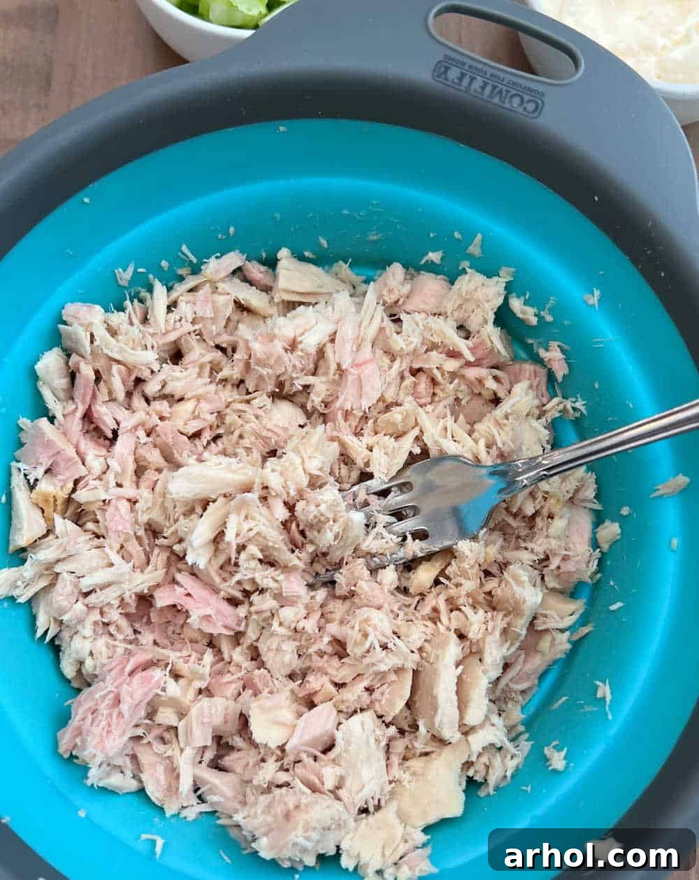A fork effortlessly flaking tender canned tuna into smaller, bite-sized pieces within a mixing bowl, preparing it for the salad.